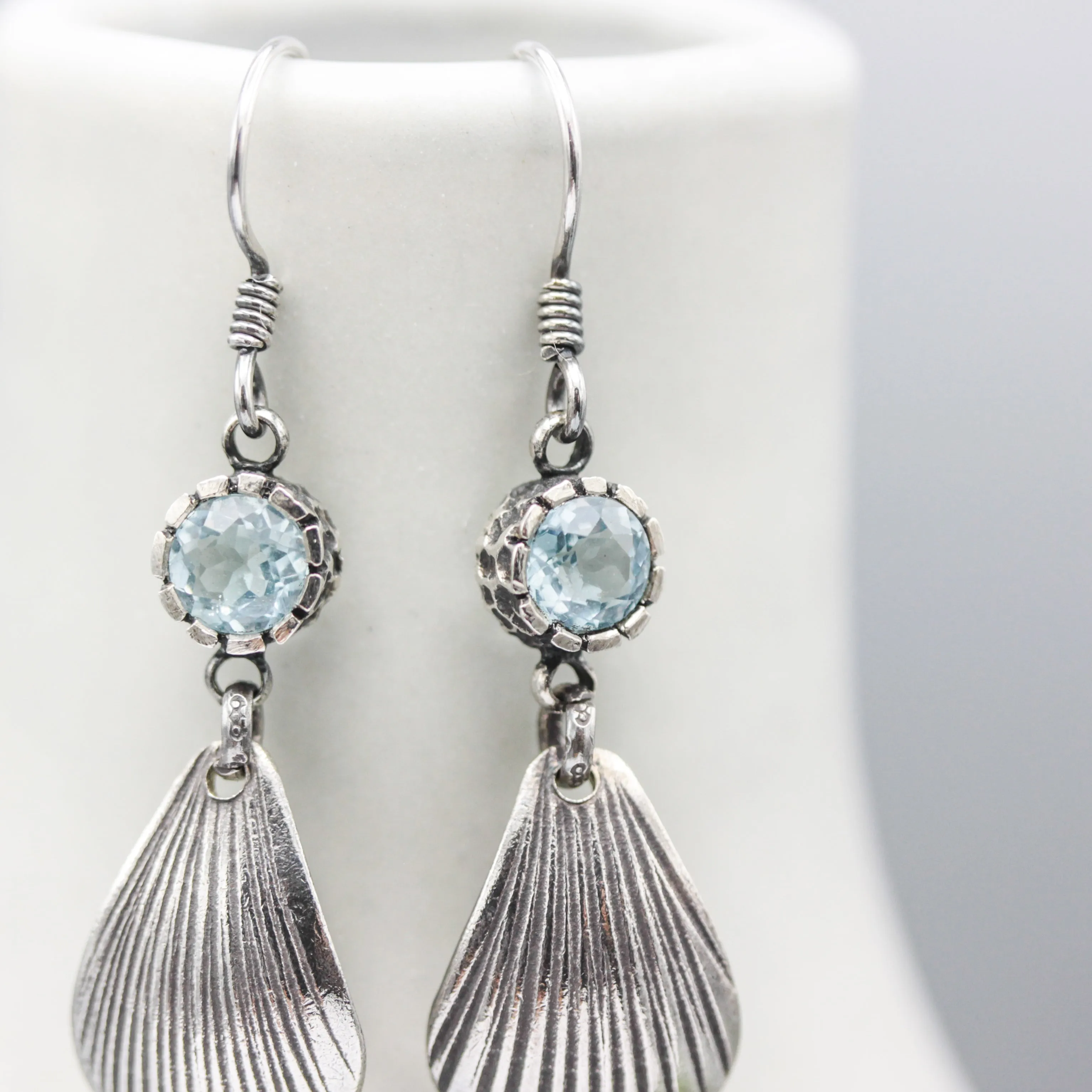 Blue topaz earrings in silver bezel setting with sterling silver shell shape on silver hooks style